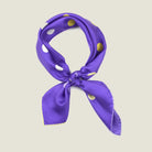 Laslett England Solitaire Violet Foulard tied in a knot. Scarf is shown in a neutral background. Scarf is inviolet silk satin with large lemon polka dots.