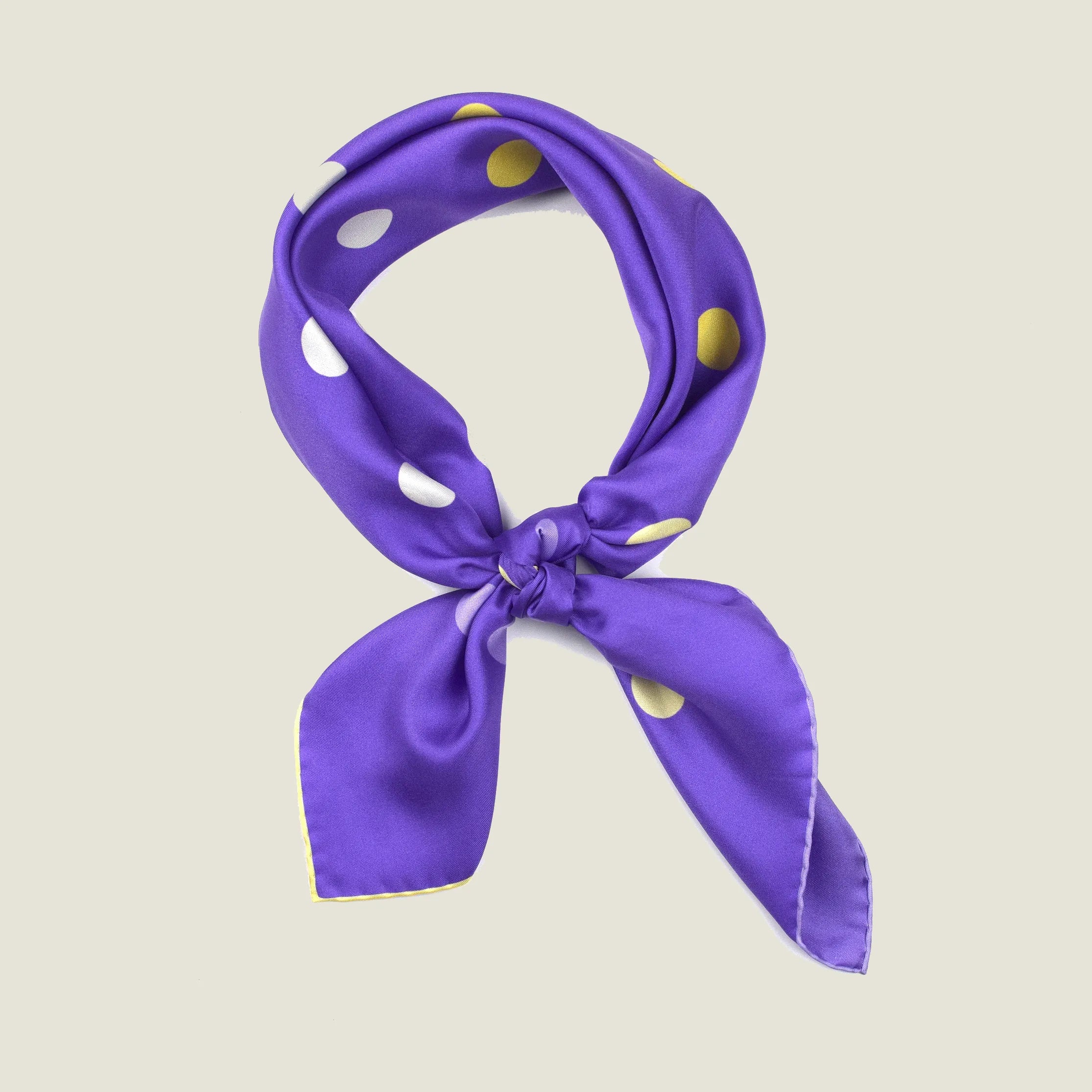 Laslett England Solitaire Violet Foulard tied in a knot. Scarf is shown in a neutral background. Scarf is inviolet silk satin with large lemon polka dots.