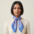 Laslett England Marettimo Cornflower Blue Bandana tied into a knot around a female model's neck. The pink pattern is inspired by botanical and coastal elements. 
