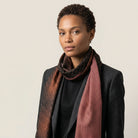Laslett England Mosaic Copper Silk Oblong worn looped at neck by female model in charcoal jacket, showing warm copper and brown trellis print on silk twill.