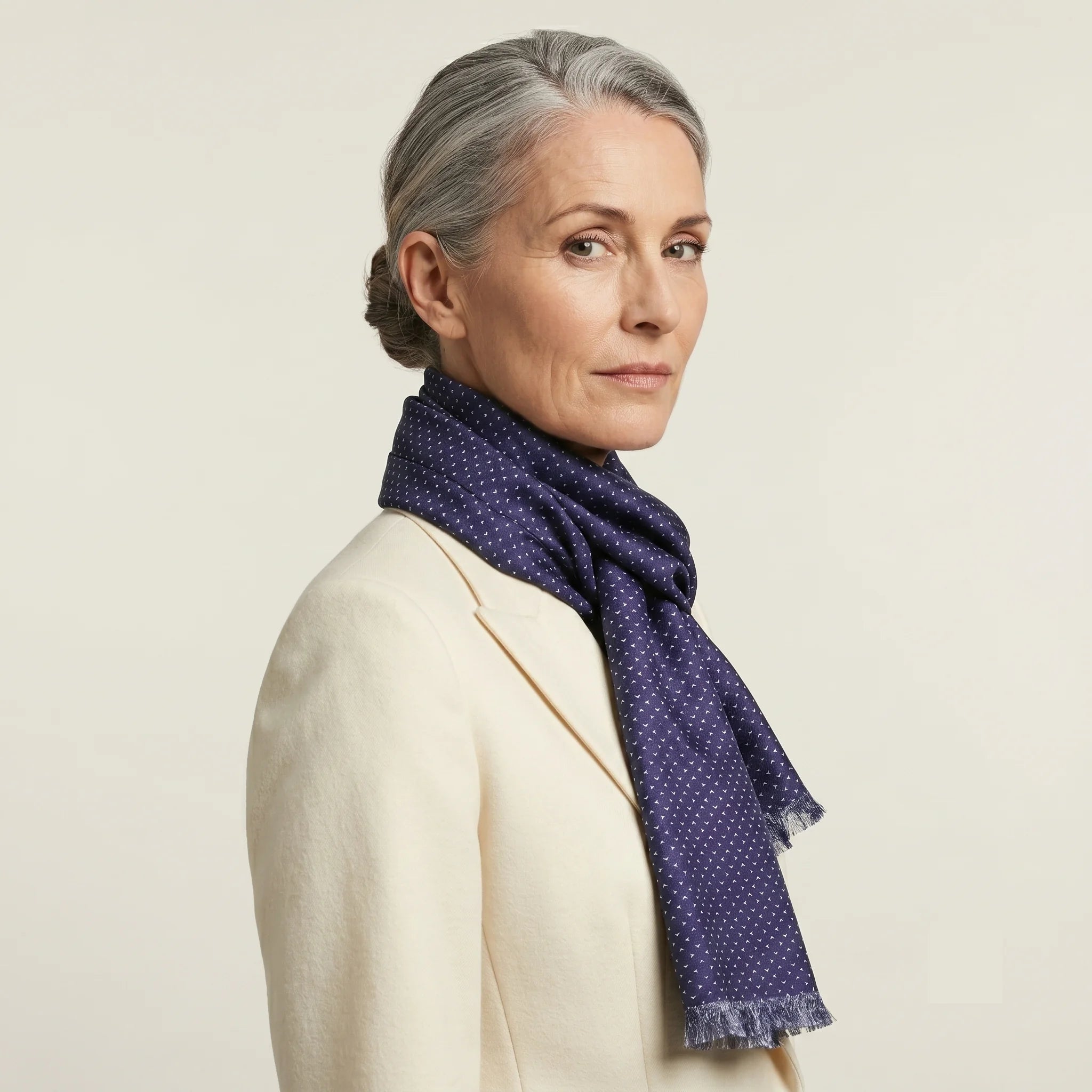 Laslett England Revival Navy Silk Oblong flat lay, 21cm x 165cm double-sided silk twill in deep navy with white pin triangle print and pin-fringed hem shown on a female model wearing a white suite. 